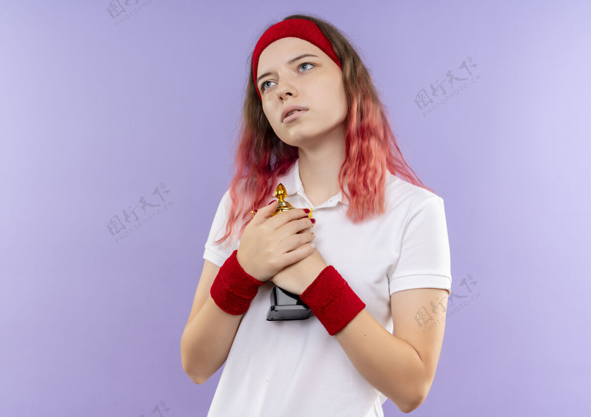 市民戴着头巾的年轻运动女性抱着她的奖杯 站在紫色的墙上 神色恍惚地望向一边看奖杯人