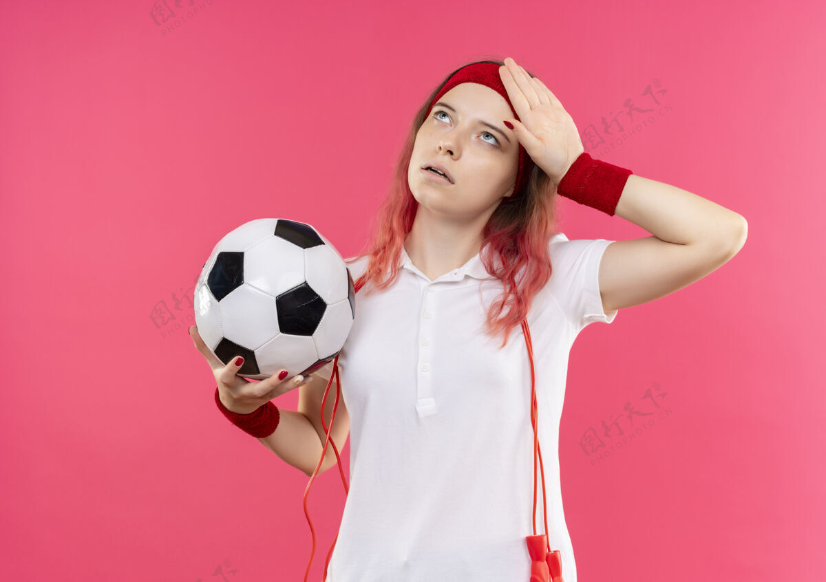 运动员站在粉红色的墙上 戴着足球头带的年轻运动型女人看起来很疲惫足球年轻运动