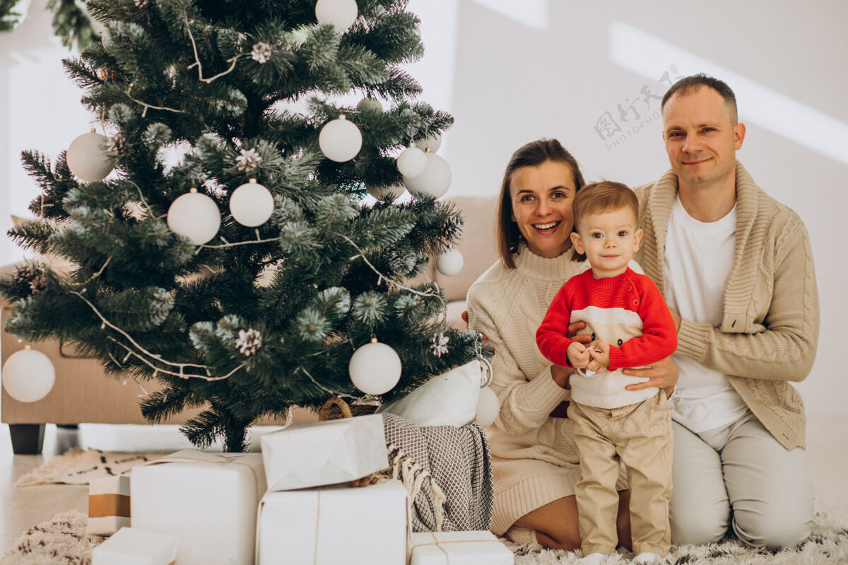女人一家人带着小儿子在家里的圣诞树旁过圣诞节妈妈圣诞礼物魔术