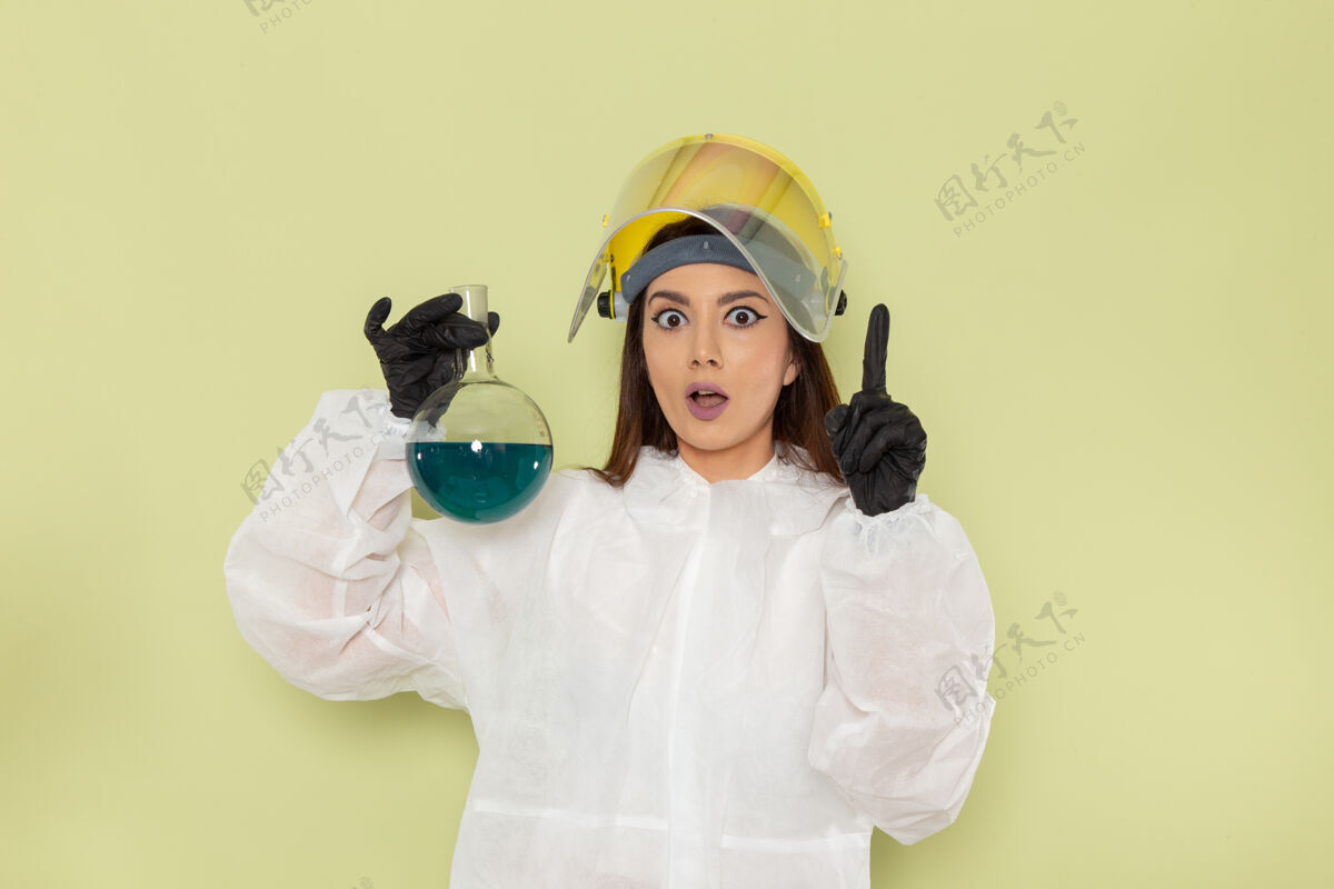 化学家正面图穿着特殊防护服的女化学家拿着绿色表面上有蓝色溶液的烧瓶女浴袍保护