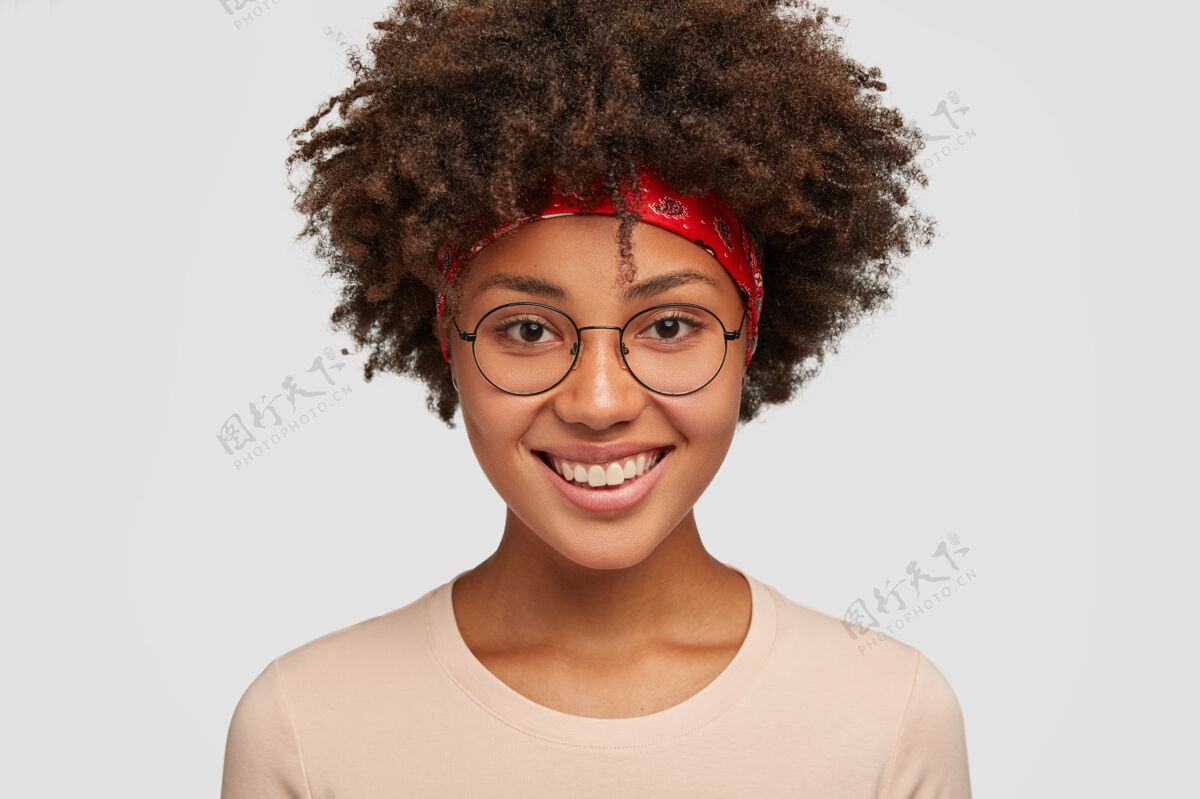 年轻人一位面容友好开朗的非洲裔美国女性的特写镜头 表情温柔 微笑愉快 为暑假的奇妙旅行感到高兴 戴着圆眼镜 穿着白色的模特表达姿势牙齿