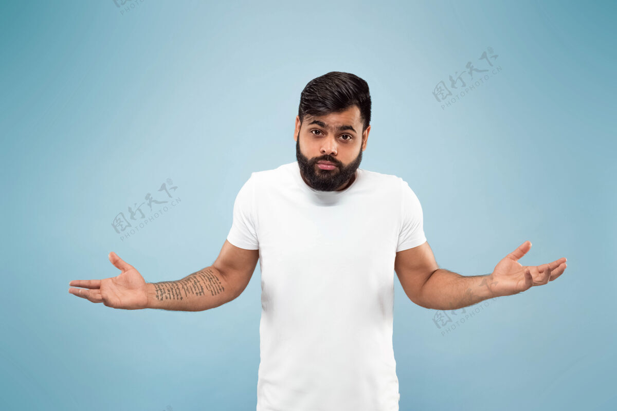 工作蓝色背景上穿着白衬衫的印度年轻人的半身特写肖像人类情感 面部表情 广告概念负面空间混乱 未知 不确定专业男人人