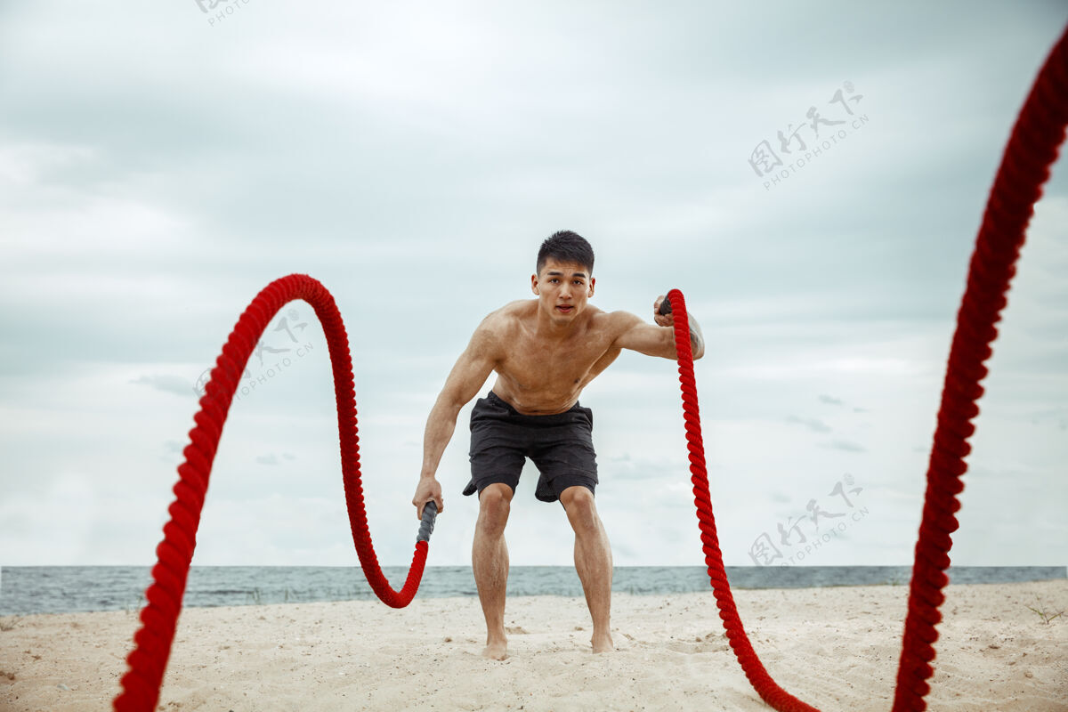 健美年轻健康的男子运动员在海滩上做深蹲男孩赤膊肌肉