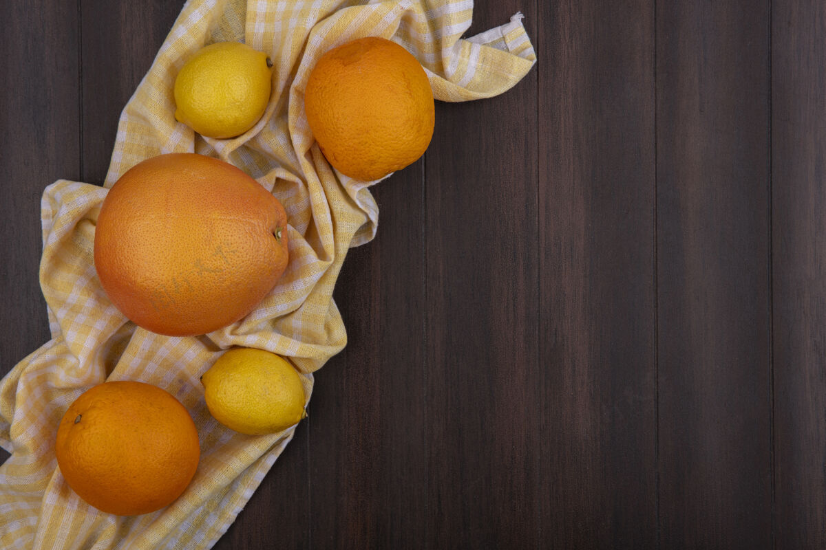 柠檬顶视图复制空间柠檬与橙色和葡萄柚黄色格子毛巾上的木制背景柠檬葡萄柚水果