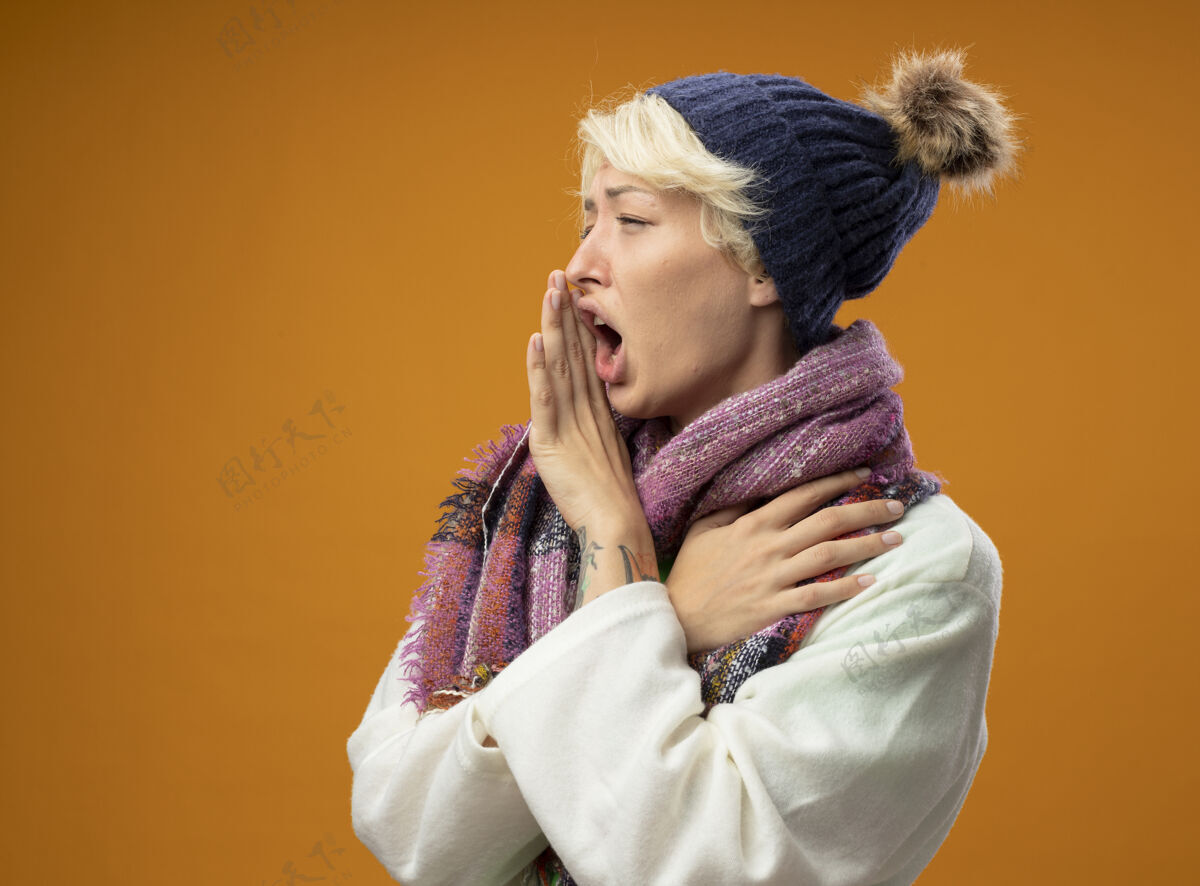 不健康生病的不健康的女人 短头发 戴着暖和的围巾 戴着帽子 站在橙色的背景上 用手靠近嘴巴大声喊叫生病帽子喊叫