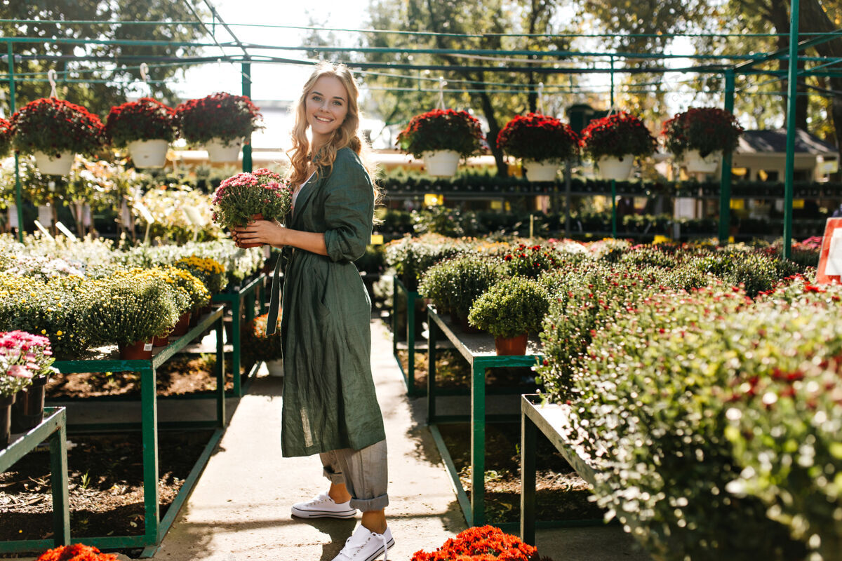 成人一位金发碧眼 笑容温柔的年轻女子 身着绿色长袍 系着腰带 正在温室里工作可爱自然花园