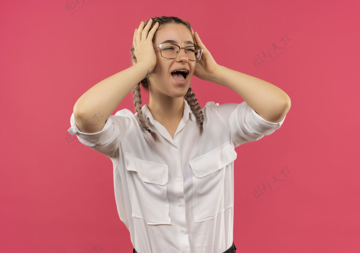 恐慌一个戴着眼镜 梳着辫子 穿着白衬衫的年轻女学生站在粉红色的墙上 一边看着一边 双手抱着头 惊恐地大叫着学生头看