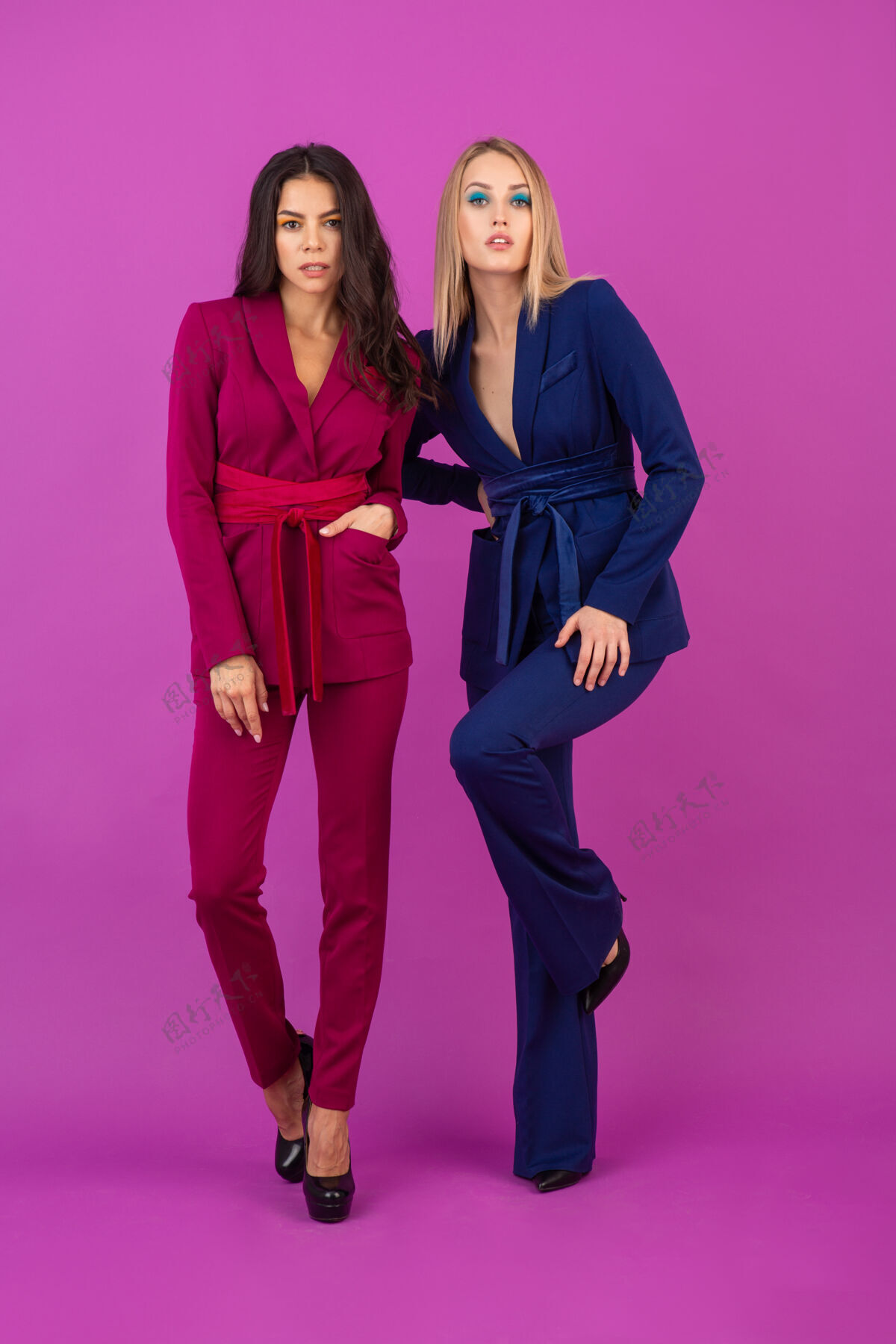 秋天高级时尚风格紫罗兰色墙壁上两位魅力四射的女士 身着紫色和蓝色的时尚多彩晚礼服 朋友们一起玩乐 时尚潮流穿着优雅多彩
