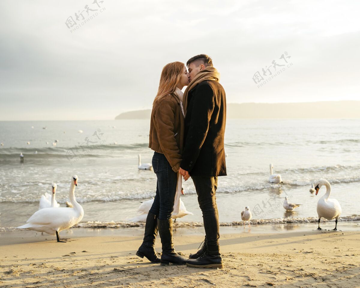 女人冬天海滩边亲吻情侣的侧视图业余爱好情侣冬天