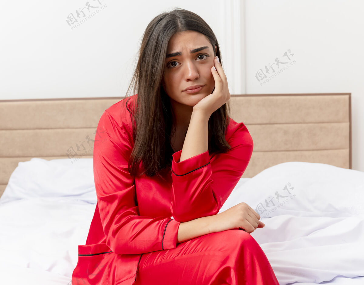 相机穿着红色睡衣在床上放松的年轻美女卧室女人坐着