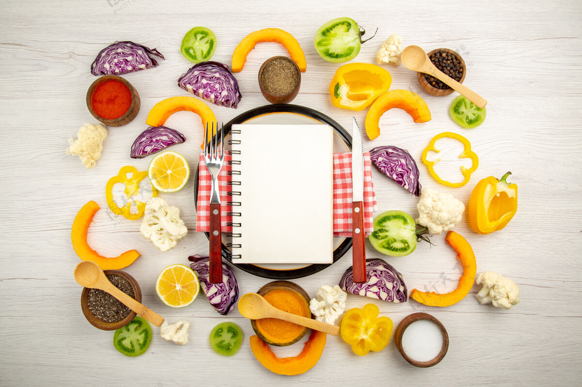 顶部俯视图食谱写在记事本上刀叉放在圆板上切蔬菜不同的香料放在碗里放在木桌上五颜六色碗叉子