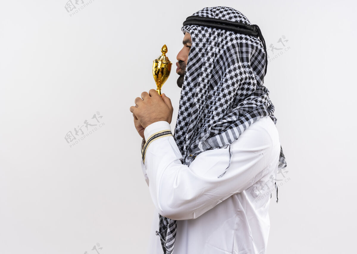 吻身着传统服装的阿拉伯男子站在白墙上亲吻奖杯男人侧身穿