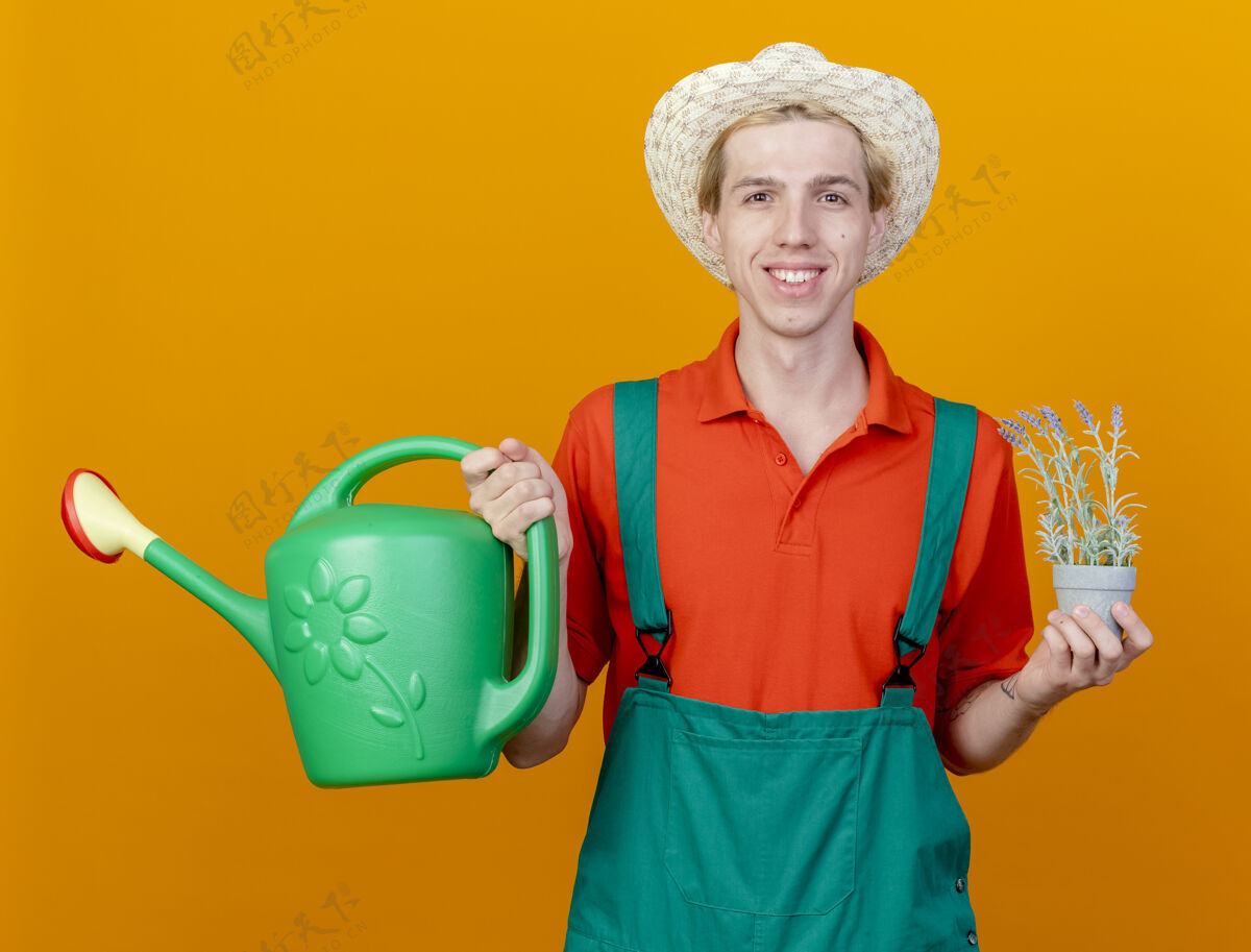 快乐快乐的年轻园丁 穿着连体衣 戴着帽子 手里拿着浇水罐男人园丁年轻