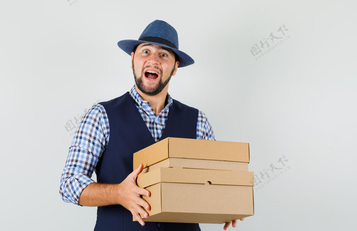 男人年轻人穿着衬衫 背心 戴着帽子 手里拿着纸板箱 看上去兴高采烈 眼前一亮年轻纸板聪明