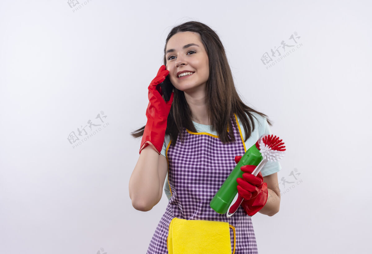 围裙穿着围裙 戴着橡胶手套 拿着清洁用品和刷子的年轻漂亮女孩微笑着讲手机刷子漂亮供应