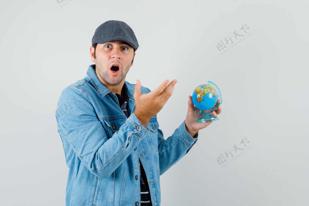 夹克年轻人手里拿着地球仪 一边看着穿着夹克 戴着帽子的相机 一脸惊讶衬衫朋友男