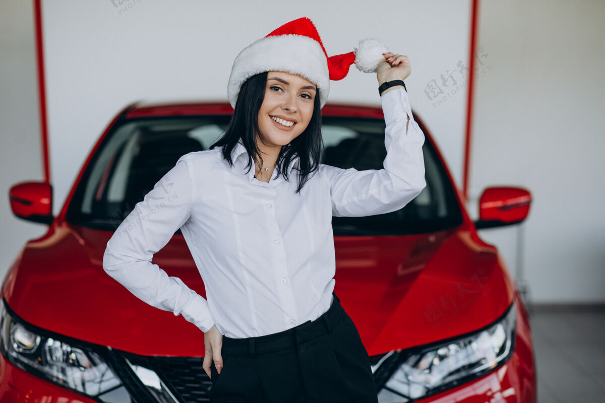 兴奋一个戴着圣诞帽的女人坐在汽车陈列室里的红色汽车旁边女性客户惊喜
