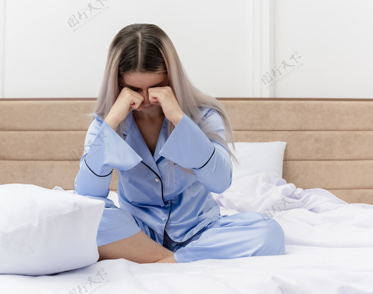 床穿着蓝色睡衣的年轻美女坐在床上揉着眼睛 在卧室的室内灯光下醒来蓝色睡衣室内
