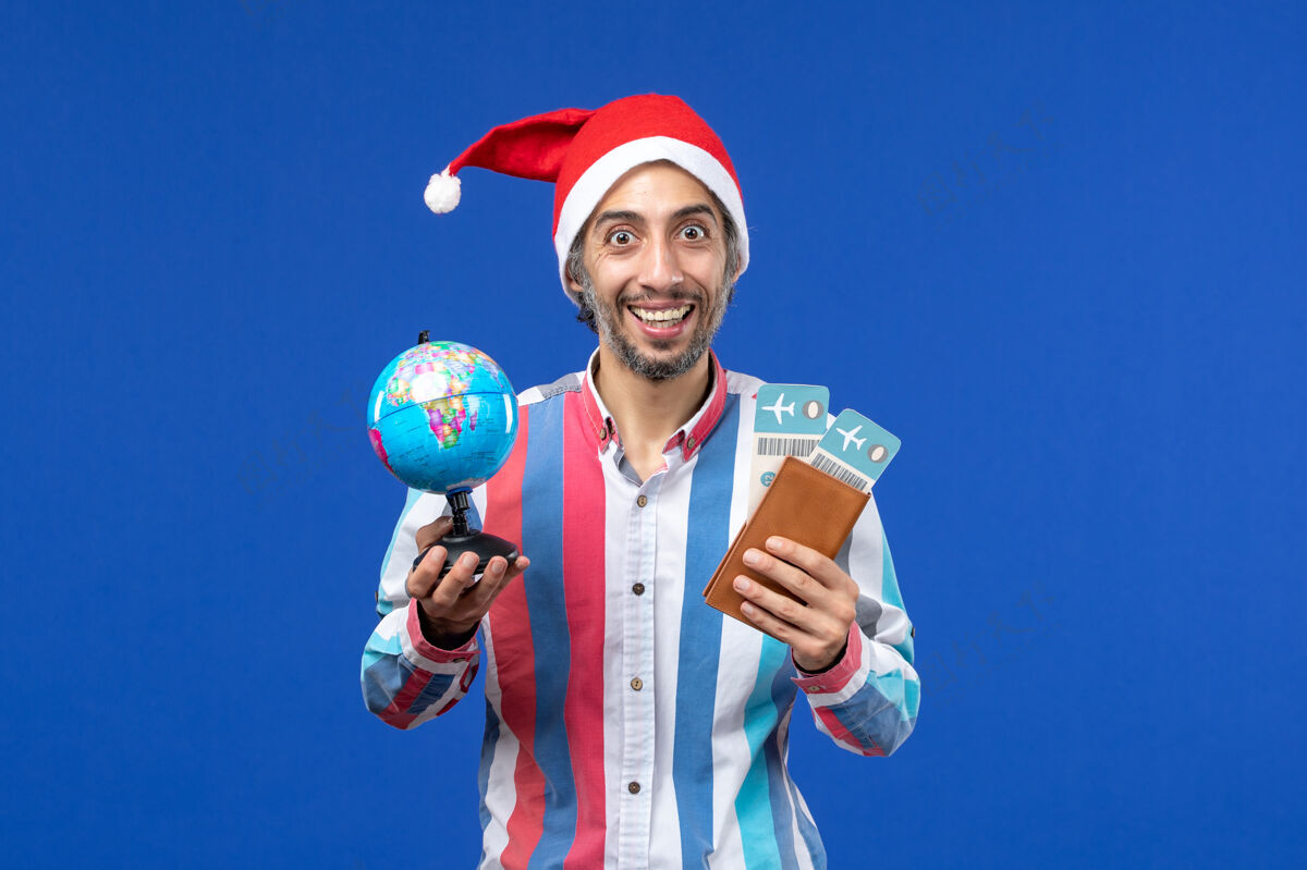 颜色前视图普通男性 带门票和地球仪 蓝色墙壁 节日新年色彩成人圣诞节喜剧演员