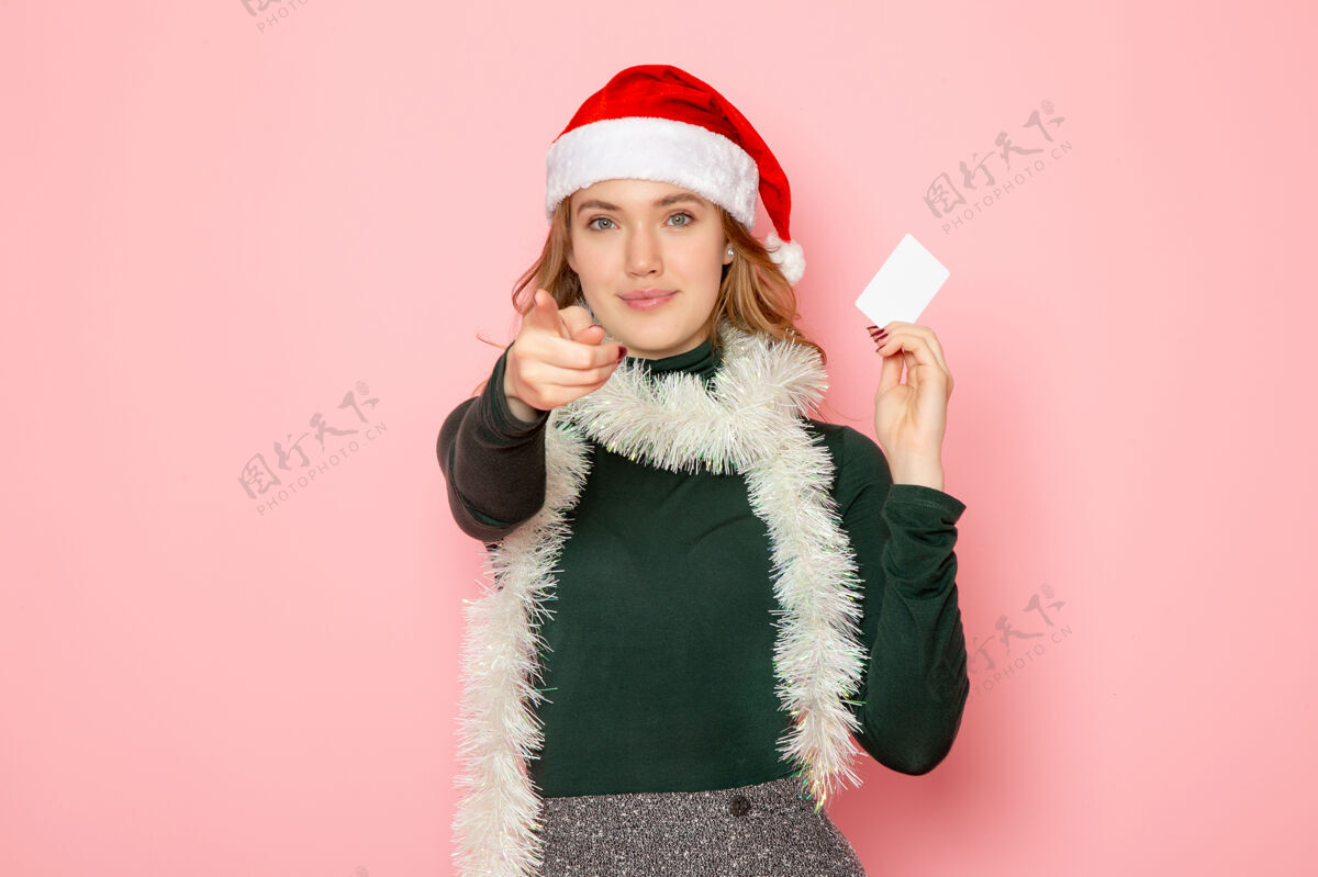 圣诞正面图年轻女性手持白色银行卡在粉色墙壁上的彩色情感模型假日圣诞新年银行年轻的女性羽毛蟒蛇