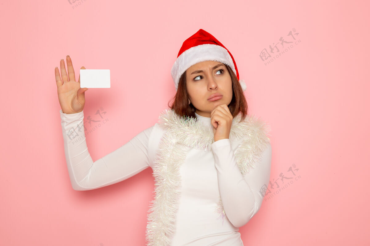 颜色正面图年轻女性手持白色银行卡在粉色墙上圣诞假期新年时尚彩钱风景年轻的女性肖像