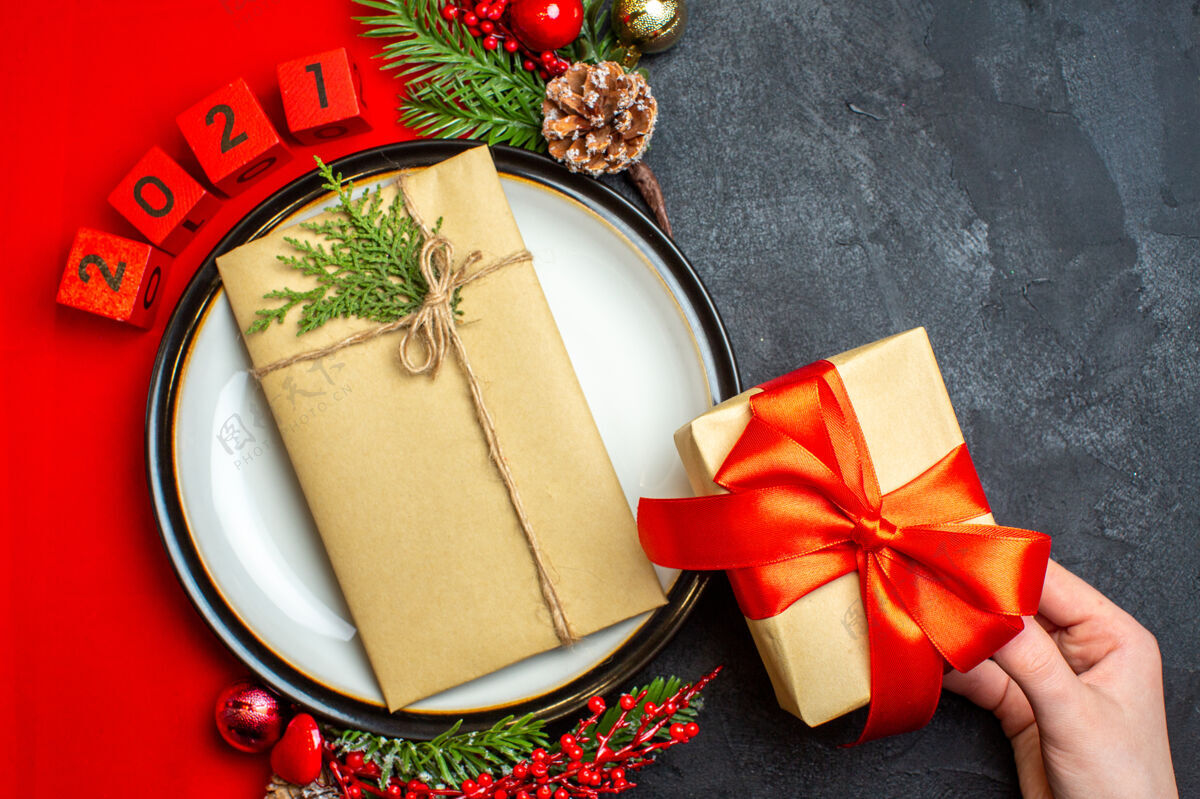 数字新年背景俯视图 餐盘上有礼物装饰配件 黑色桌子上的红色餐巾上有杉木树枝和数字风景圣诞节冷杉
