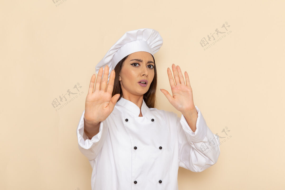 前面身穿白色厨师服的年轻女厨师在浅白墙上摆姿势的正面图护士女性工作