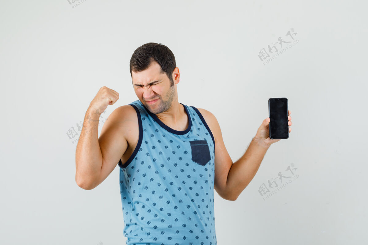 手机身穿蓝色单品的年轻人手持手机 摆出胜利者的姿态 看上去很开心胡须休闲信心
