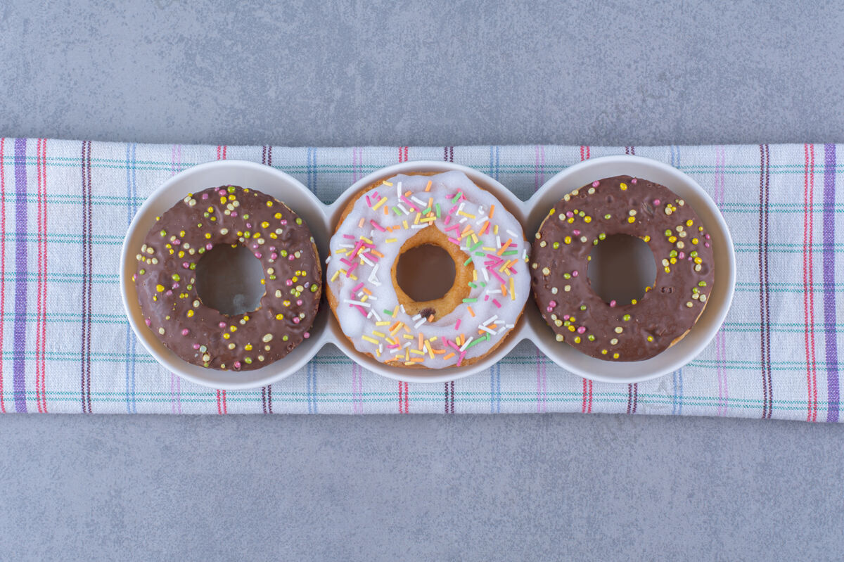 吃的三个甜甜的巧克力甜甜圈 在桌布上撒上五颜六色的糖食物桌布可食用的