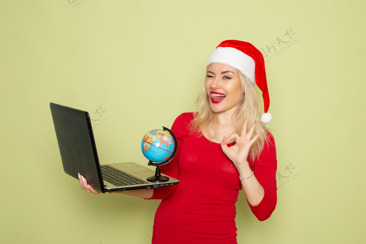 磁盘骑师正面图漂亮的女人拿着地球仪和笔记本电脑在绿色的墙上度假情绪圣诞雪新年的颜色漂亮的女性成人地球仪
