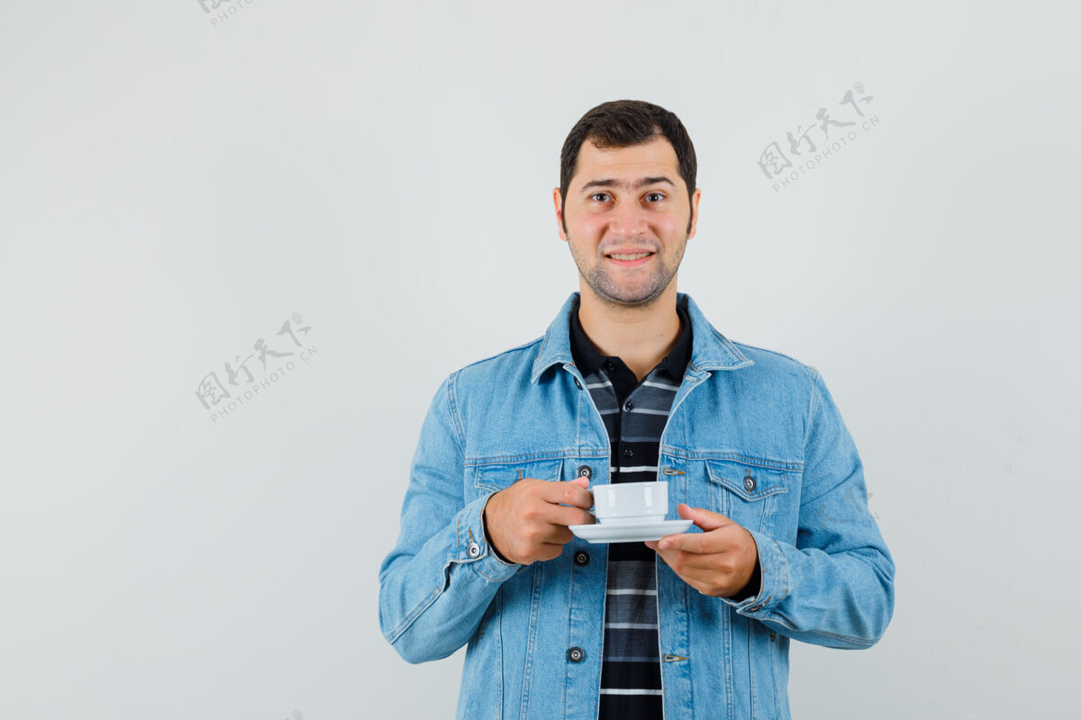 男人年轻人手里拿着一杯茶 穿着t恤衫 夹克衫 看上去兴高采烈自信夹克成功