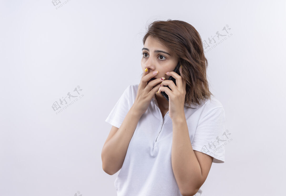 马球一个穿着白色马球衫的短发女孩一边用手捂着嘴一边用手机讲话 震惊了站手短裤