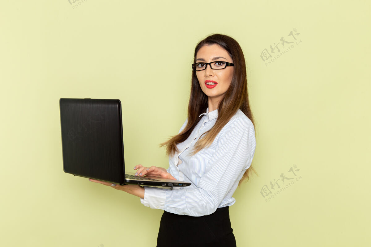 商务穿着白衬衫和黑裙子的女上班族在浅绿色办公桌上使用笔记本电脑的前视图上班族生意繁忙人衬衫工人