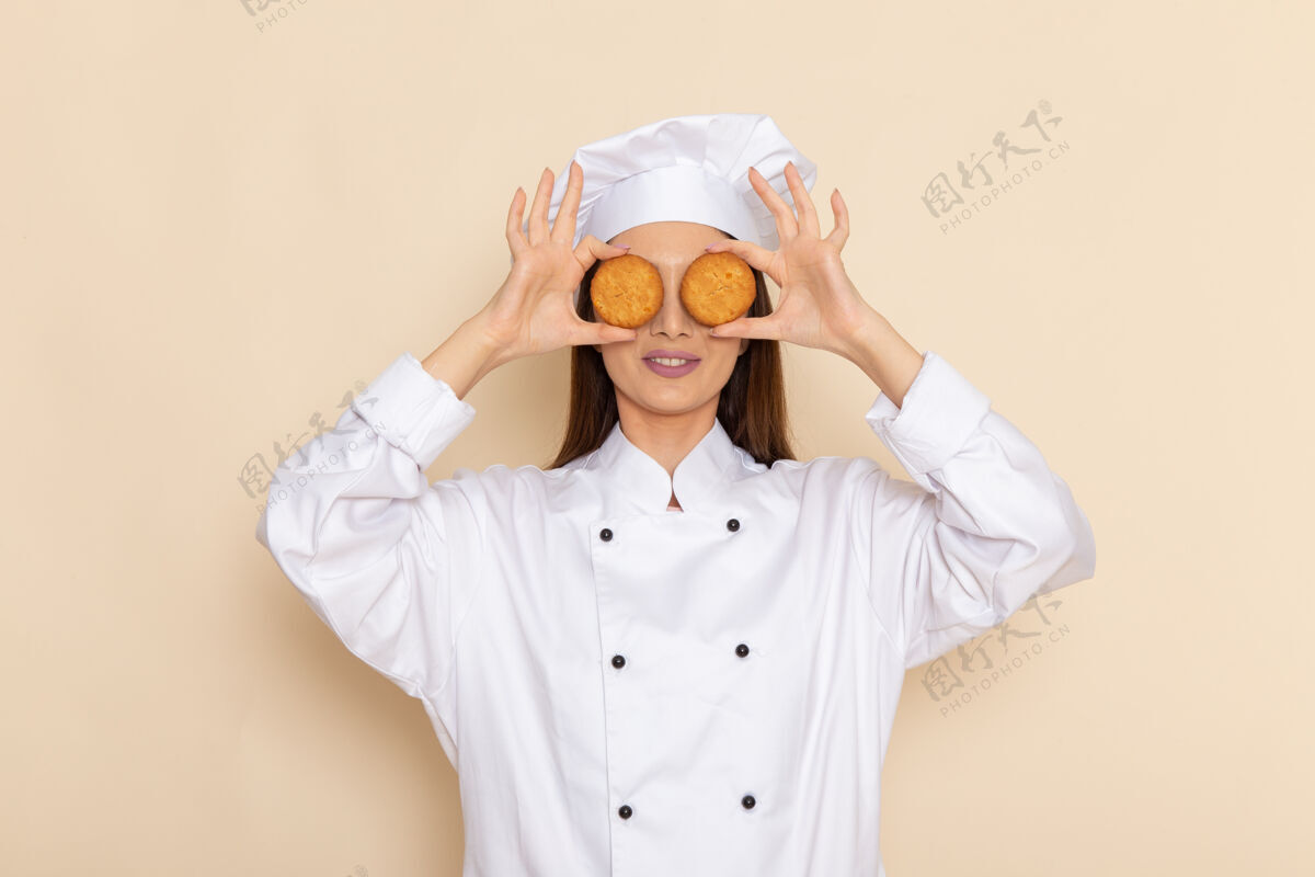 年轻身穿白色厨师服的年轻女厨师正拿着甜饼站在白墙上厨房工人女性