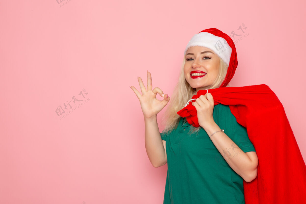 风景正面图年轻女性提着红包带着礼物上了粉红色的墙壁模型假日圣诞老人新年照片彩色圣诞老人年轻的女性携带颜色