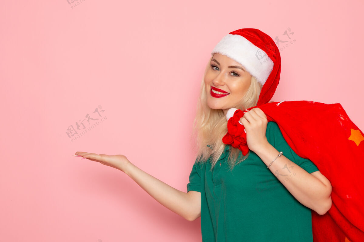 肖像正面图年轻女性拎着红包带着礼物在粉色墙上度假模特圣诞新年彩照美丽圣诞微笑