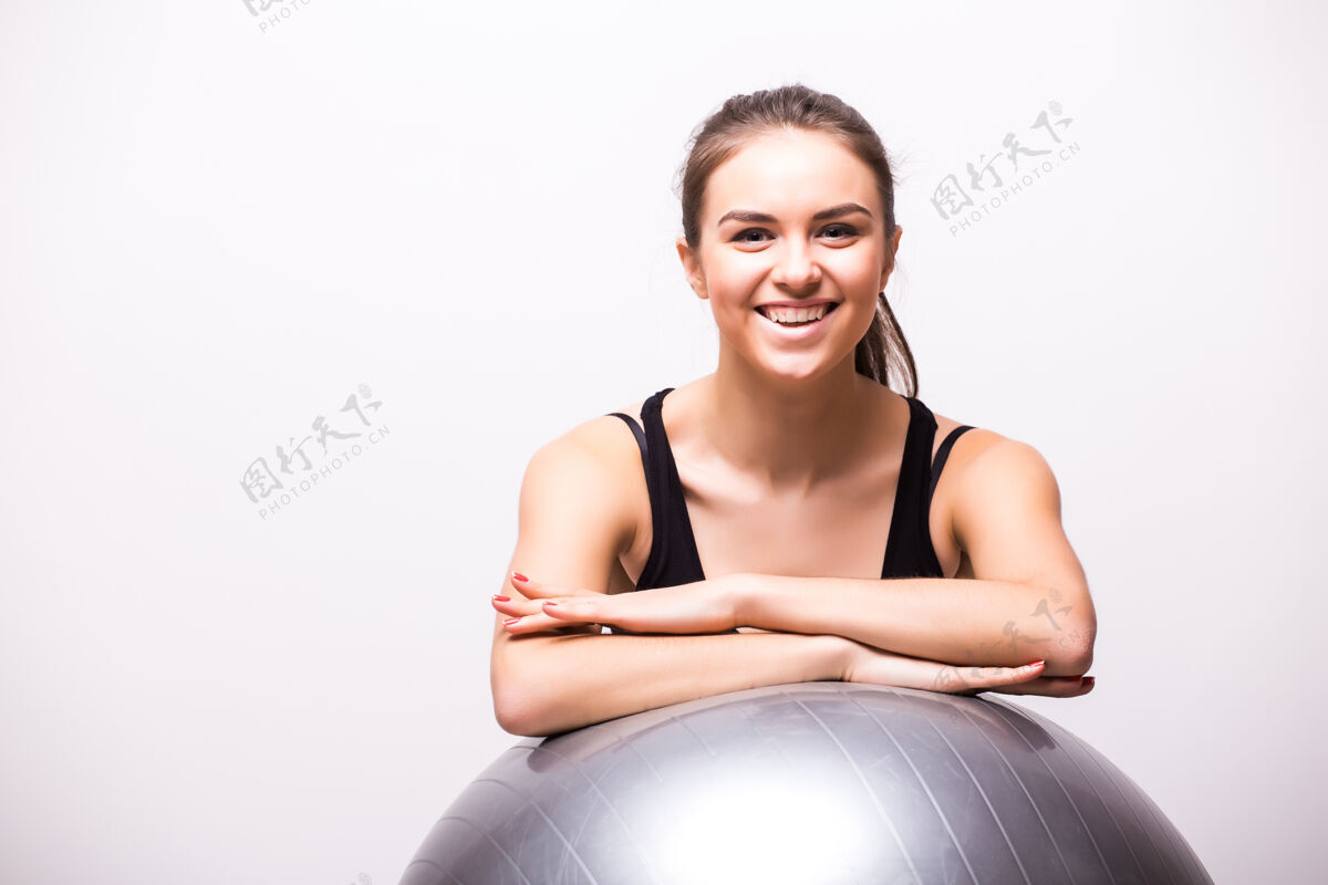 球一个年轻的女人拿着一个孤立在白墙上的球锻炼肌肉设备漂亮