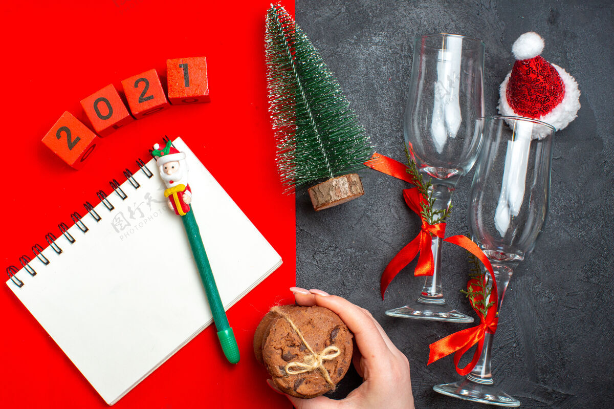 螺丝刀手持螺旋笔记本和圣诞树玻璃高脚杯的俯视图数字手持堆叠在黑暗和红色背景上的饼干手工工具设备设备