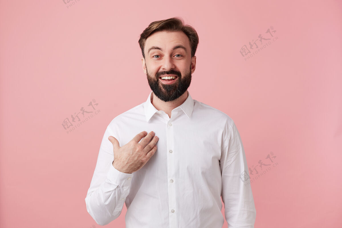 心情快乐迷人的年轻黑发男子 留着时髦的发型 穿着白衬衫 站在粉红色的墙上 愉快地向前方张望衣服男士朋友