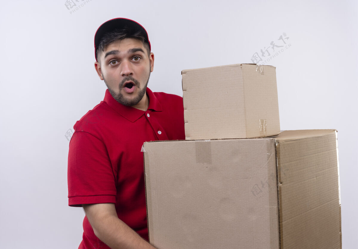 帽子年轻的送货员穿着红色制服 戴着帽子 手里拿着大纸箱 看上去既惊讶又惊奇纸板站着送货