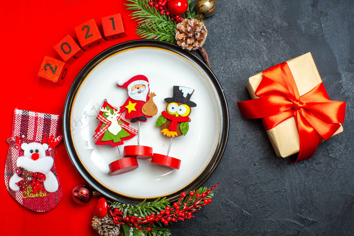 容器餐盘装饰配件俯视图杉木树枝和数字圣诞袜放在一张红色餐巾旁边的礼物放在一张黑色的桌子上圣诞节盘子餐巾