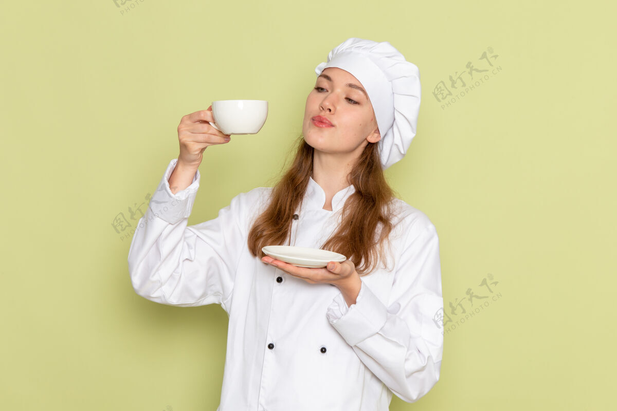 女性身着白色厨师服的女厨师正拿着一杯咖啡站在绿色的墙上烹饪微笑肖像