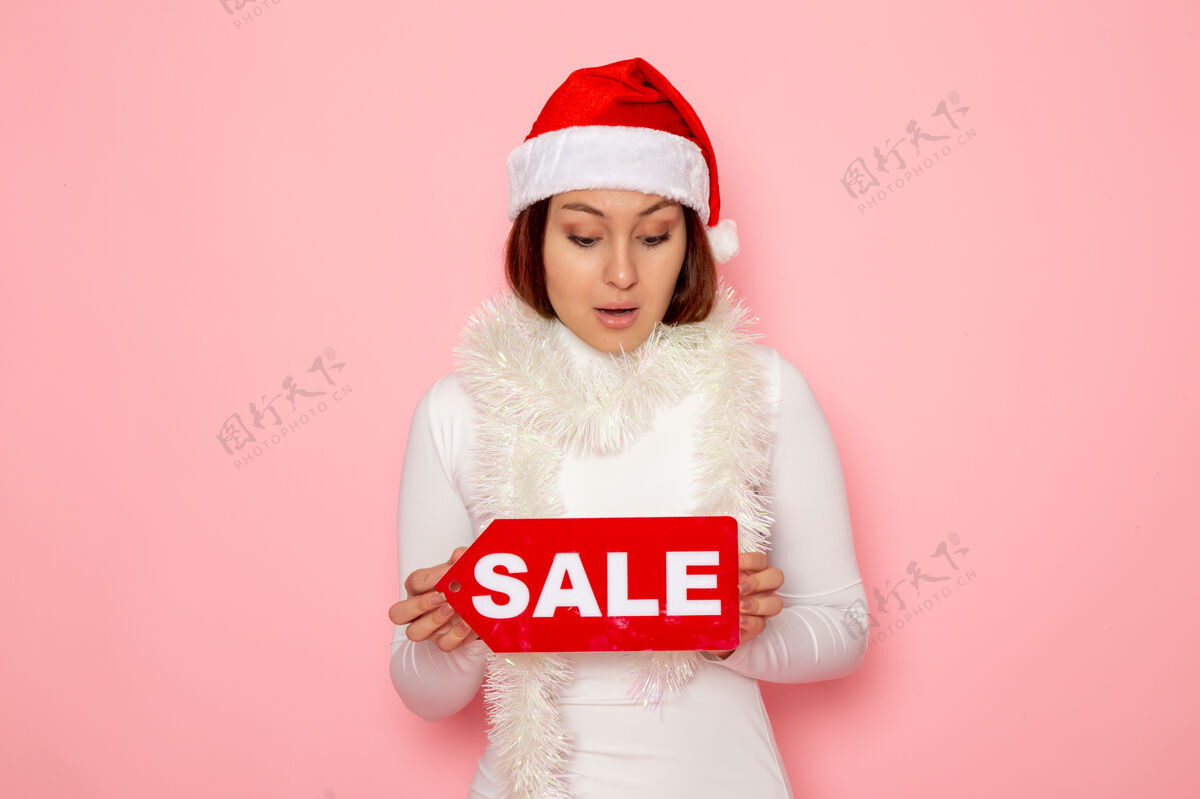 雪正面图年轻女子手持卖写在粉红色墙上的人物情感色彩雪地圣诞新年假期微笑资本颜色