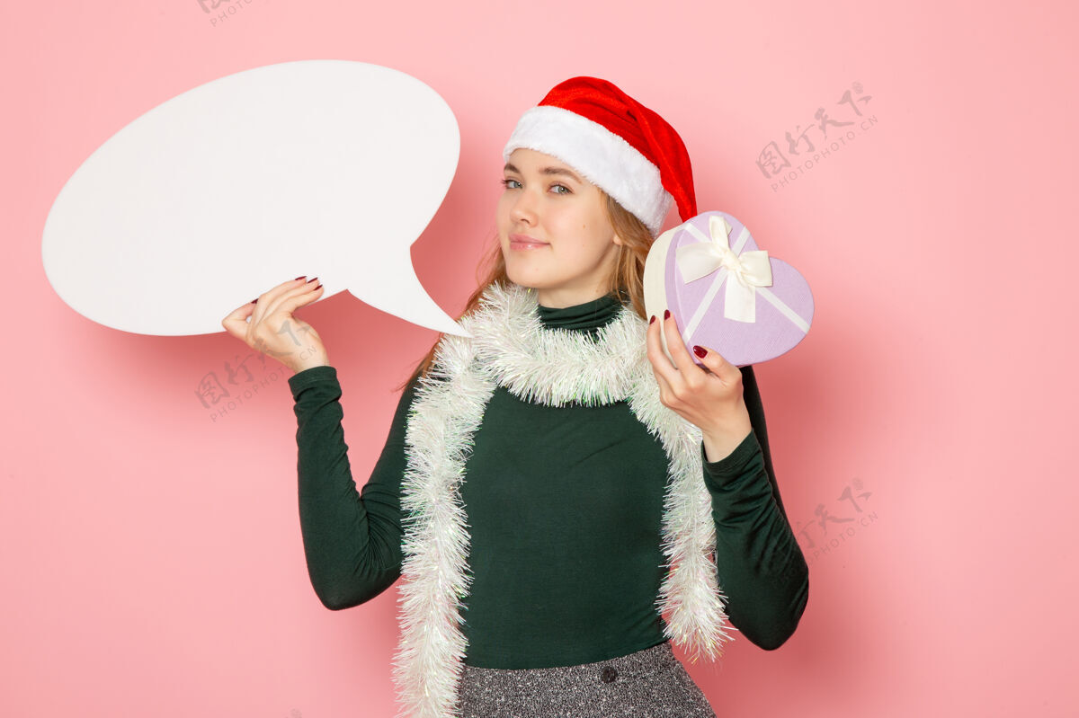 颜色正面图年轻女性手持白色大招牌 在粉色墙上呈现模特节日圣诞新年的色彩情感小年轻的女性快乐