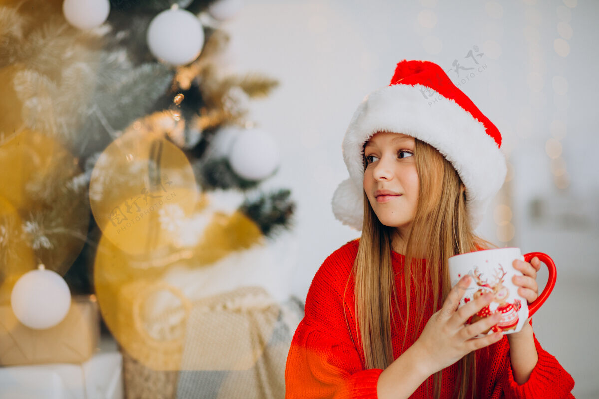 年轻在圣诞树旁喝可可的女孩礼物平安夜饮用