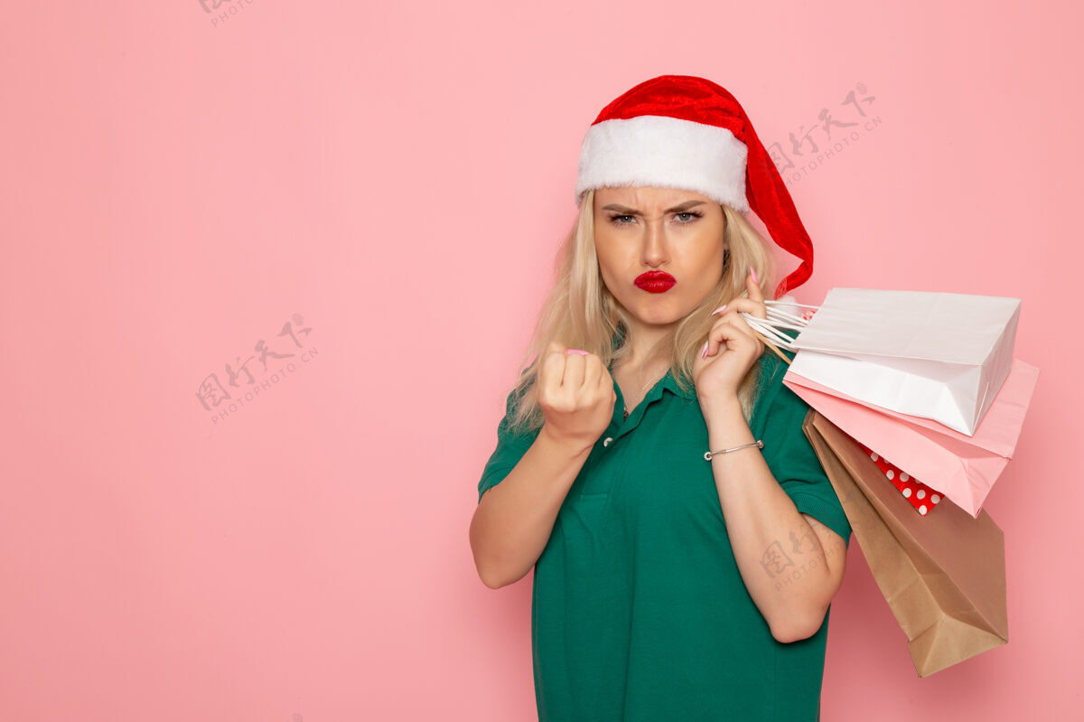 色彩正面图：年轻女性手拿圣诞礼物 包装在粉红色墙上的模型节日新年照片的颜色圣诞风景美丽