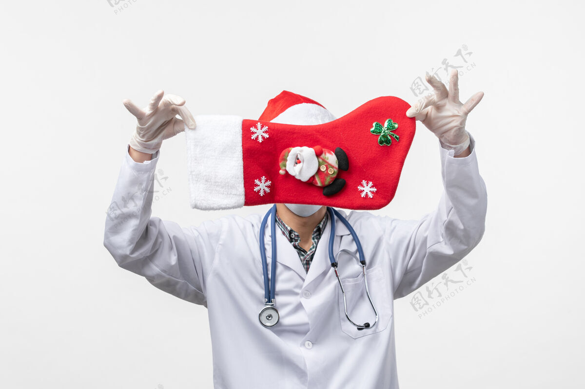 冠状病毒正面图：男医生拿着节日袜子在白墙上戴着圣诞健康病毒医生男人肖像