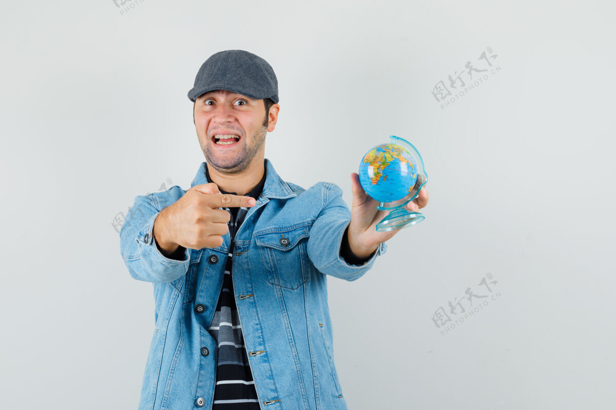 衬衫穿着夹克 戴着帽子的年轻人指着地球 看上去很乐观乐观自信成功