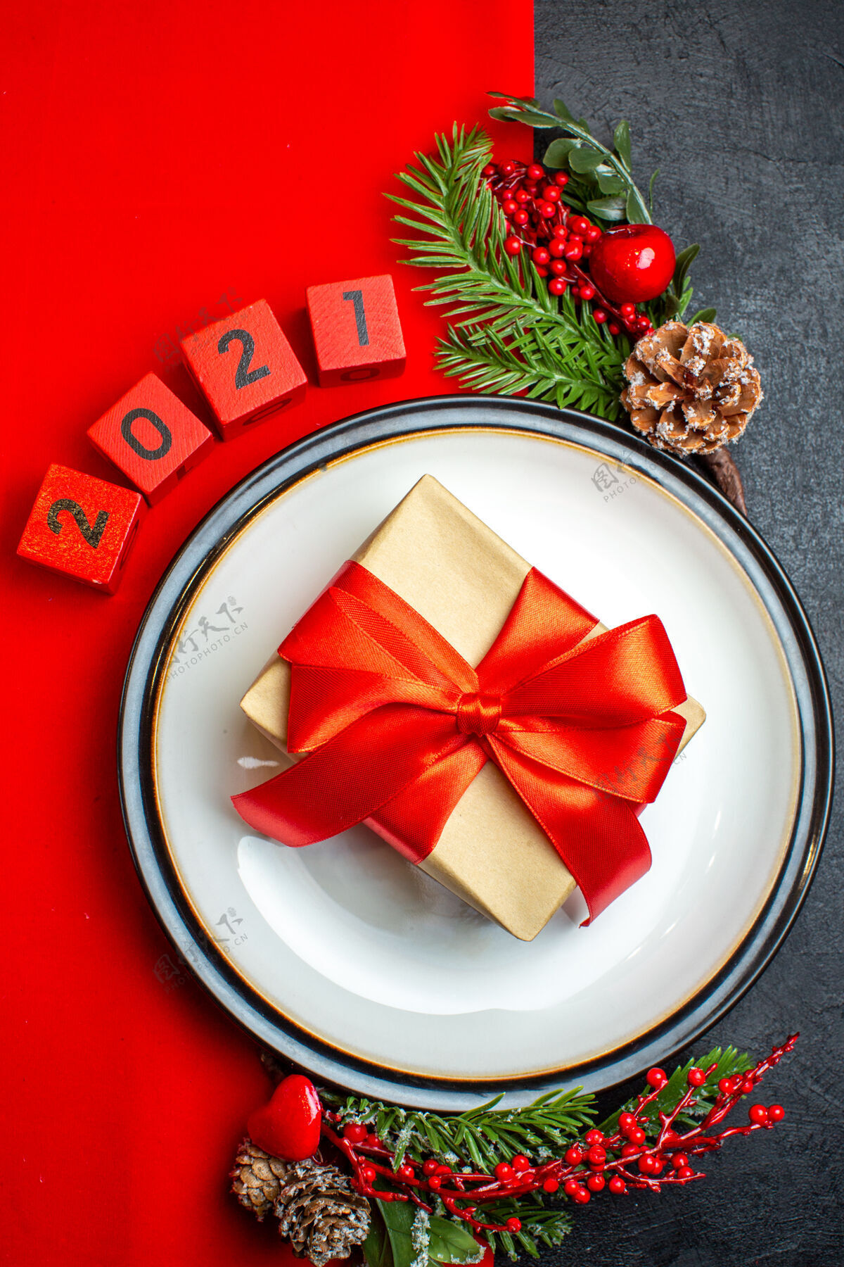 餐盘新年背景用漂亮的礼品装饰在一个餐盘上 配件杉木枝和数字放在一张红色餐巾上 黑色的桌子上俯视树枝风景冷杉