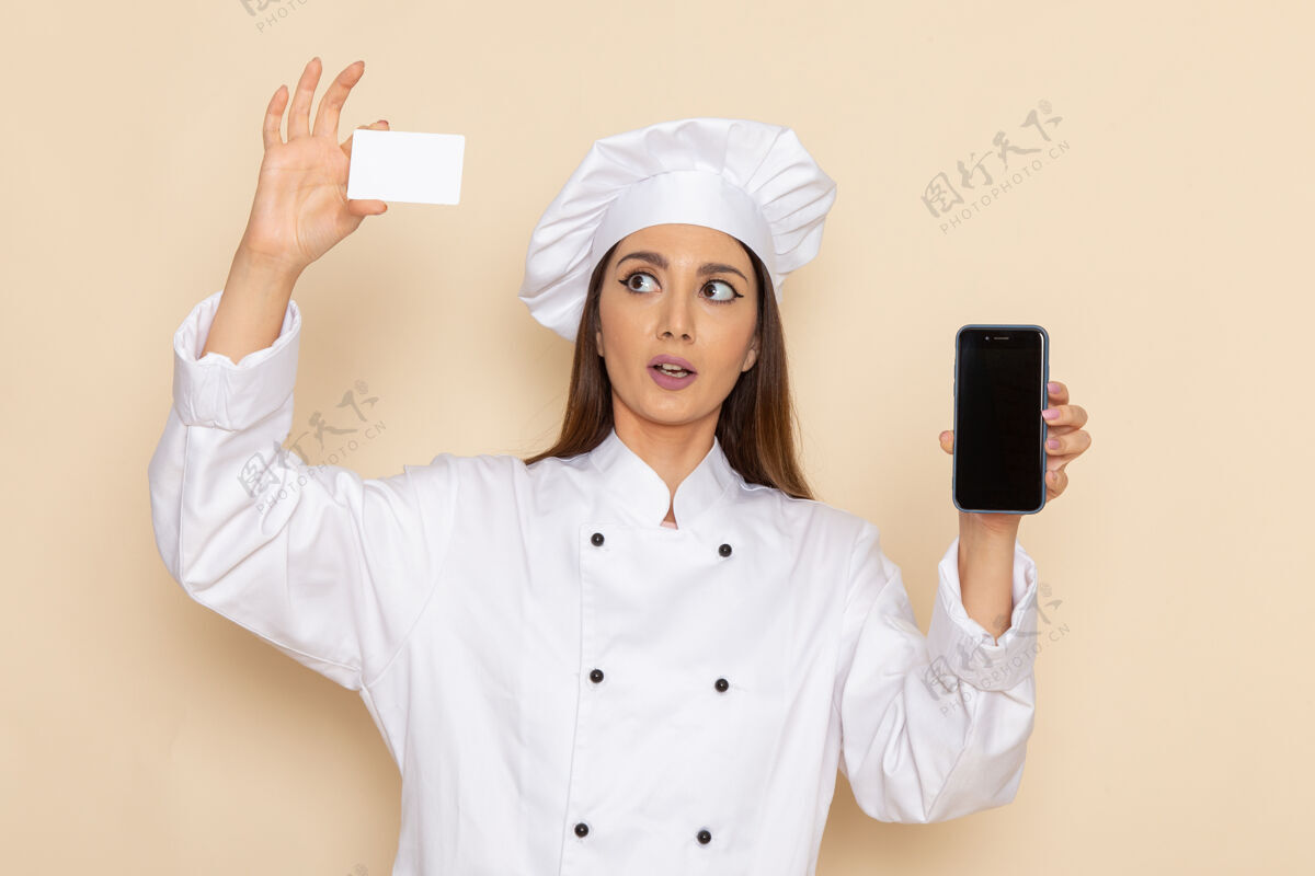 工作身穿白色厨师服的年轻女厨师的正视图 在浅白的墙上拿着电话和名片举行秘书女性
